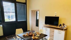 A compact living space with a dining table, four chairs, a TV on a wooden cabinet, and a door with a window. - B&B l'angoletto (Trebisacce)