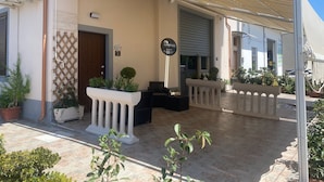 A hotel entrance with a covered patio, outdoor seating, and potted plants. - B&B l'angoletto (Trebisacce)