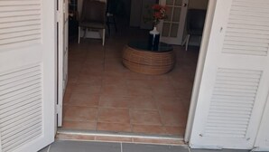 Ein offenes Doppeltür zum Raum mit Deckenventilator, einem Korbstuhl und einem kleinen Tisch mit Blumen in einer Vase.