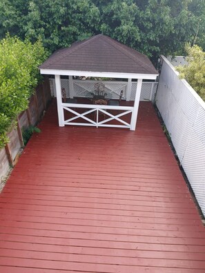 A covered patio area with a red wooden deck, white railing, and a dark roof.