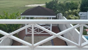 Blick von einer überdachten Außenfläche mit weißer Brüstung, einem Pavillon und einer Terrasse mit Grill.