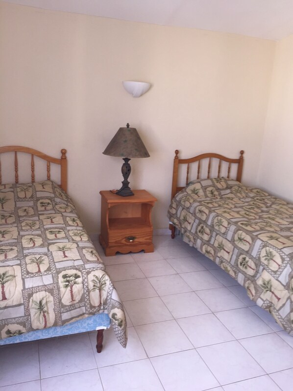 A bedroom with two single beds, a nightstand with a lamp, and a wall-mounted light fixture.