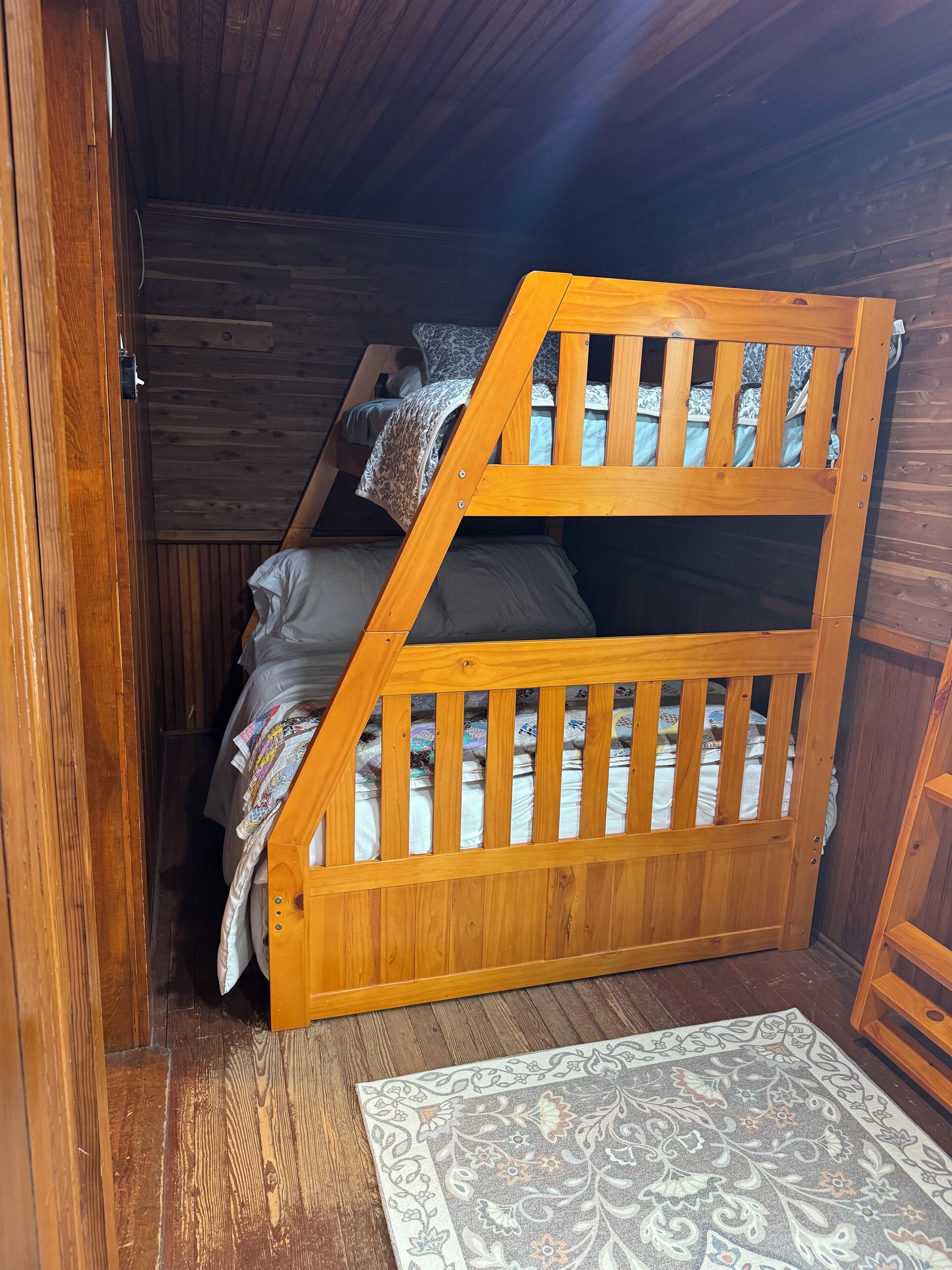 Un lit superposé en bois dans une pièce aux murs en bois et ornée d’un tapis à motifs sur le sol.
