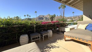 An outdoor patio with a sofa, chairs, and a table, overlooking a mountainous landscape with palm trees. - Desert Retreat in Rancho Mirage – Bright, Stylish Condo with Resort Amenities (Rancho Mirage)