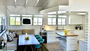 A modern kitchen with white cabinets, a wooden countertop, and a hanging light fixture. There is a dining area with a table and chairs, and a sofa with patterned cushions. - Desert Retreat in Rancho Mirage – Bright, Stylish Condo with Resort Amenities (Rancho Mirage)