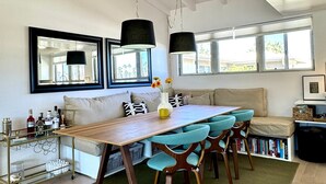 A modern dining area with a wooden table, teal chairs, and a green rug. - Desert Retreat in Rancho Mirage – Bright, Stylish Condo with Resort Amenities (Rancho Mirage)