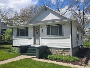 A single-story house with a front porch, a door with a wreath, and a small front yard with a stone wall and plants. - Charming 2-bedroom cottage minutes away from Linn Pier on Lake Geneva (Lake Geneva)
