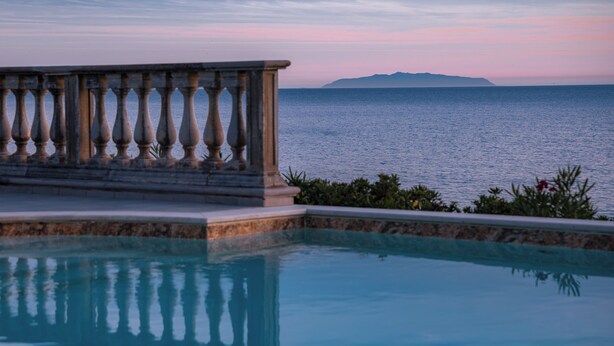 Une piscine bordée d’une balustrade en pierre, offrant une vue sur la mer.