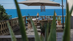 Un espace de restauration en plein air avec une table et des chaises, un grand parasol et une vue sur la mer.