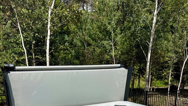 Un bain à remous doté d’un couvercle, entouré d’une clôture et d’arbres.