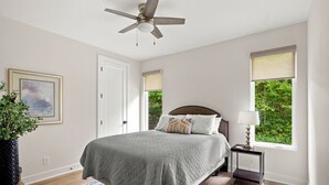Une chambre à coucher avec un lit, un ventilateur de plafond, une table de chevet avec une lampe, une fenêtre donnant sur un beau paysage et un tableau encadré accroché au mur.