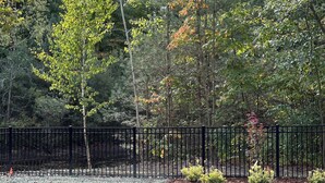 Une zone recouverte de gravier, délimitée par une clôture en métal noir, et entourée d’arbres aux feuilles vertes et aux couleurs automnales.