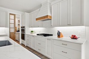 A modern kitchen with white cabinetry, a wooden accent, and a fruit bowl on the counter. - SOMETHING FOR EVERYONE,  New 3+ BR, 4 Bath, Ranch, Game Rm, Fenced Yd & Pond (Fennville)