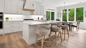 Une cuisine moderne avec des meubles blancs, un îlot central doté de tabourets de bar et une grande fenêtre offrant une vue sur la verdure.