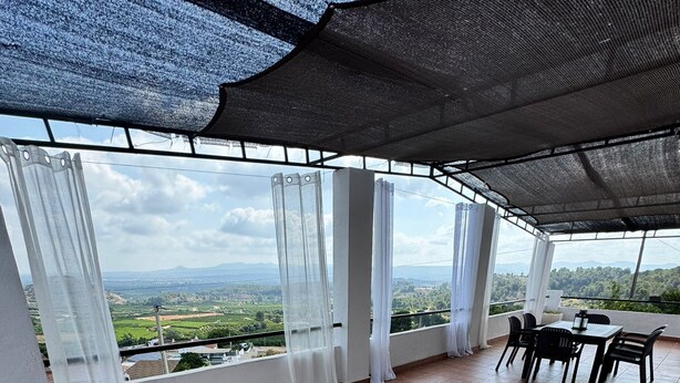 A spacious balcony with a view of a green landscape and mountains. There is a table and chairs set up for dining. - House with Jacuzzi in the mountains. (Valencia)