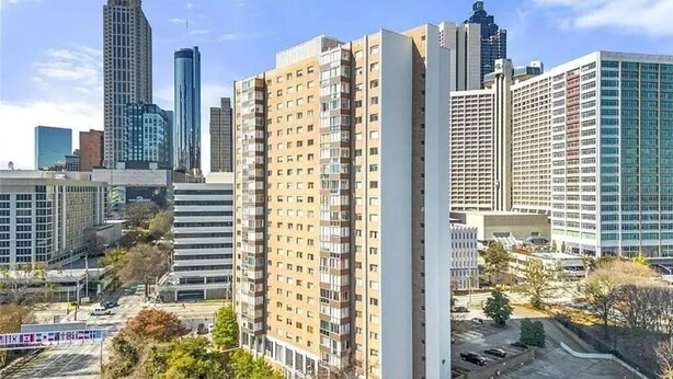 Ein Hochhaus mit mehreren Stockwerken, umgeben von anderen hohen Gebäuden, in einer städtischen Umgebung.