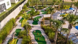 Un campo de golf con varios putting greens, palmeras y sillones de descanso.