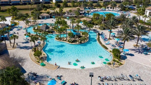 Un resort con piscina central, varias zonas de descanso y un barrio residencial al fondo.
