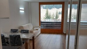 Ett modernt kök med matplats, trägolv och utsikt över träd genom ett stort fönster.