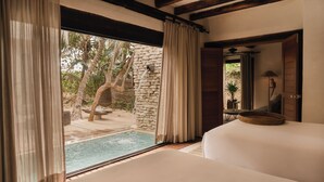 A bedroom with a large window, a stone wall, and a view of a pool and trees. - Casa Chukum 4BR by Aldea Canzul (Tulum)