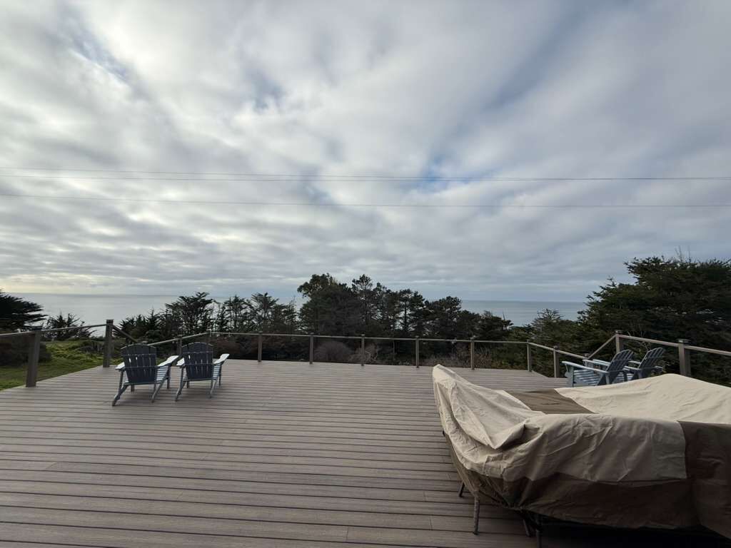 A wooden deck with chairs and a covered area, overlooking a natural landscape with trees and a body of water.