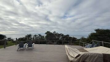A wooden deck with chairs and a covered area, overlooking a natural landscape with trees and a body of water.