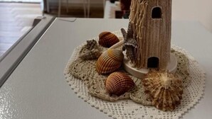 A small lighthouse model on a table with a doily, surrounded by seashells. - Coro & Bentu  (Alghero)