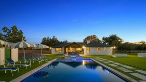 A swimming pool with lounge chairs, a house with a patio, and a well-maintained lawn. - Camp Starlight–Luxe Villa w/ Pickleball, Pool, Spa (Dripping Springs)