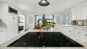 A modern kitchen with white cabinets, a black induction cooktop, and a large island with a sink. - Camp Starlight–Luxe Villa w/ Pickleball, Pool, Spa (Dripping Springs)