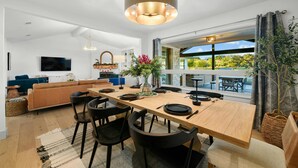 A modern kitchen with a wooden table set for dining, a large window with a view of the outdoors, and a hanging light fixture. - Camp Starlight–Luxe Villa w/ Pickleball, Pool, Spa (Dripping Springs)