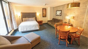 A hotel room with a bed, a sofa, a dining table with chairs, and a lamp. - Ski-in/ski-out unit 1128 for 4 people @Snowbird for New Year's week, 12/27-1/3 (Snowbird)