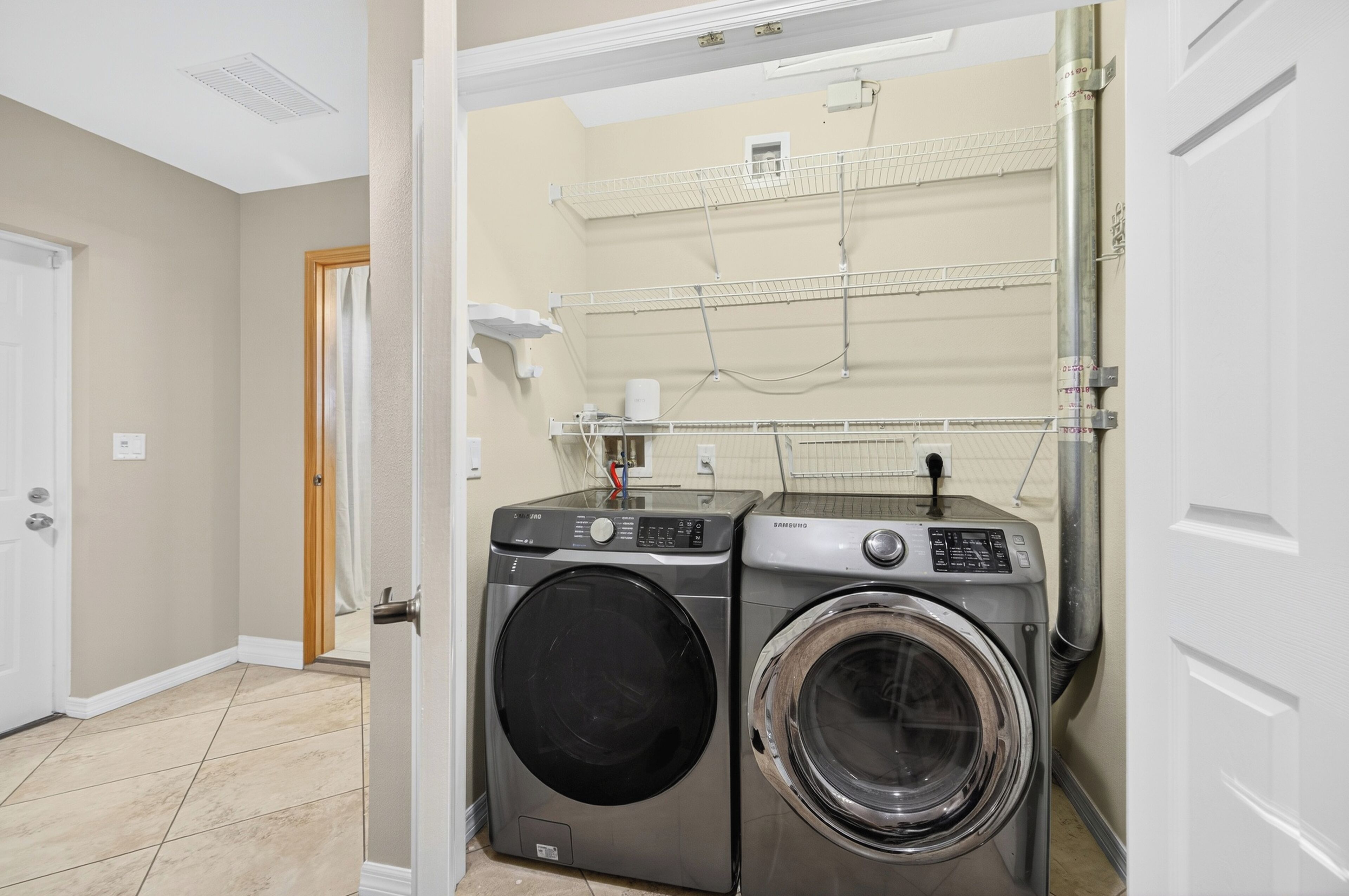 A laundry room with two stacked washers and dryers, a door, and a tiled floor.