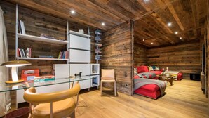 Interior acogedor de una cabaña con techo de madera, un escritorio de cristal con una silla, un sofá rojo y una estantería llena de libros.