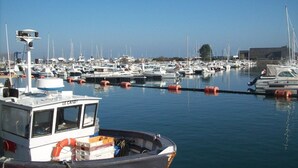 Una marina con varias embarcaciones amarradas, un barco llamado "LE CANOT" en primer plano y un cielo azul despejado.