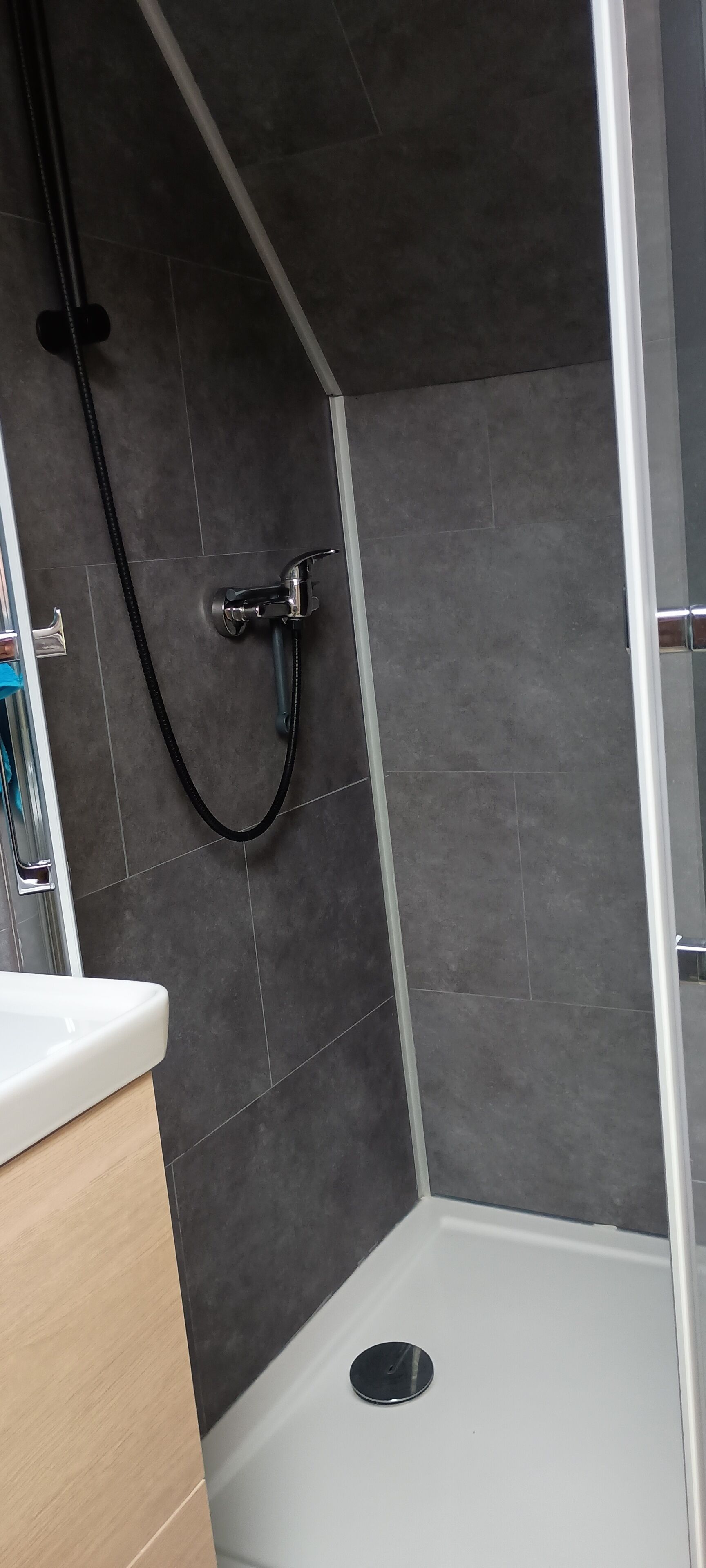 A modern bathroom with a shower area, a white sink, and a wooden vanity.