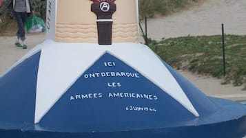 Ein Denkmal mit einem Sternmuster, einer geflügelten Fackel und Inschriften, darunter "KM 00", "VOI DE LA LIBERTE 1944" und "ICI ONT DEBARQUE LES ARMEES AMERICAINES 6 JUIN 1944".