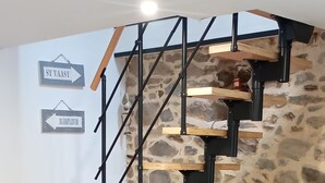 Una escalera con escalones de madera y barandillas negras que conduce a un muro de piedra. Hay una mesa con sillas y un letrero que indica las direcciones a 'St. Vaast' y 'Barfleur'.
