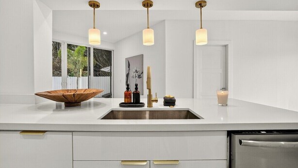 A modern kitchen with a white countertop, stainless steel sink, and three pendant lights. - Delray Oasis: Heated Pool, Spa, Arcade, Sleeps 10 (Delray Beach)