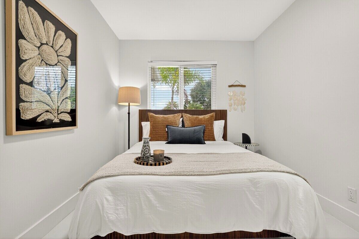 A bedroom with a bed, a bedside lamp, a window, and a wall-mounted artwork.