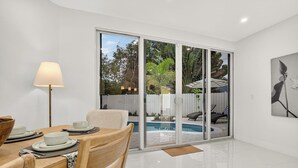 A modern dining area with a table set for four, a floor lamp, and a view of a swimming pool through glass doors. - Delray Oasis: Heated Pool, Spa, Arcade, Sleeps 10 (Delray Beach)