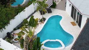 A swimming pool with a unique shape, surrounded by a white fence, and a small hot tub. - Delray Oasis: Heated Pool, Spa, Arcade, Sleeps 10 (Delray Beach)