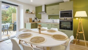 A modern kitchen with green cabinets, a white dining table with placemats, and a view of the outdoors. - Cosy house with terrace in the heart of Munster (Munster)