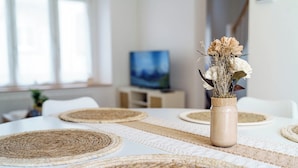 A dining table with woven placemats, a vase with flowers, and a television in the background. - Cosy house with terrace in the heart of Munster (Munster)