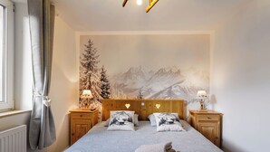 A bedroom with a mountain mural, a bed with patterned bedding, two bedside tables with lamps, and a radiator. - Cosy house with terrace in the heart of Munster (Munster)
