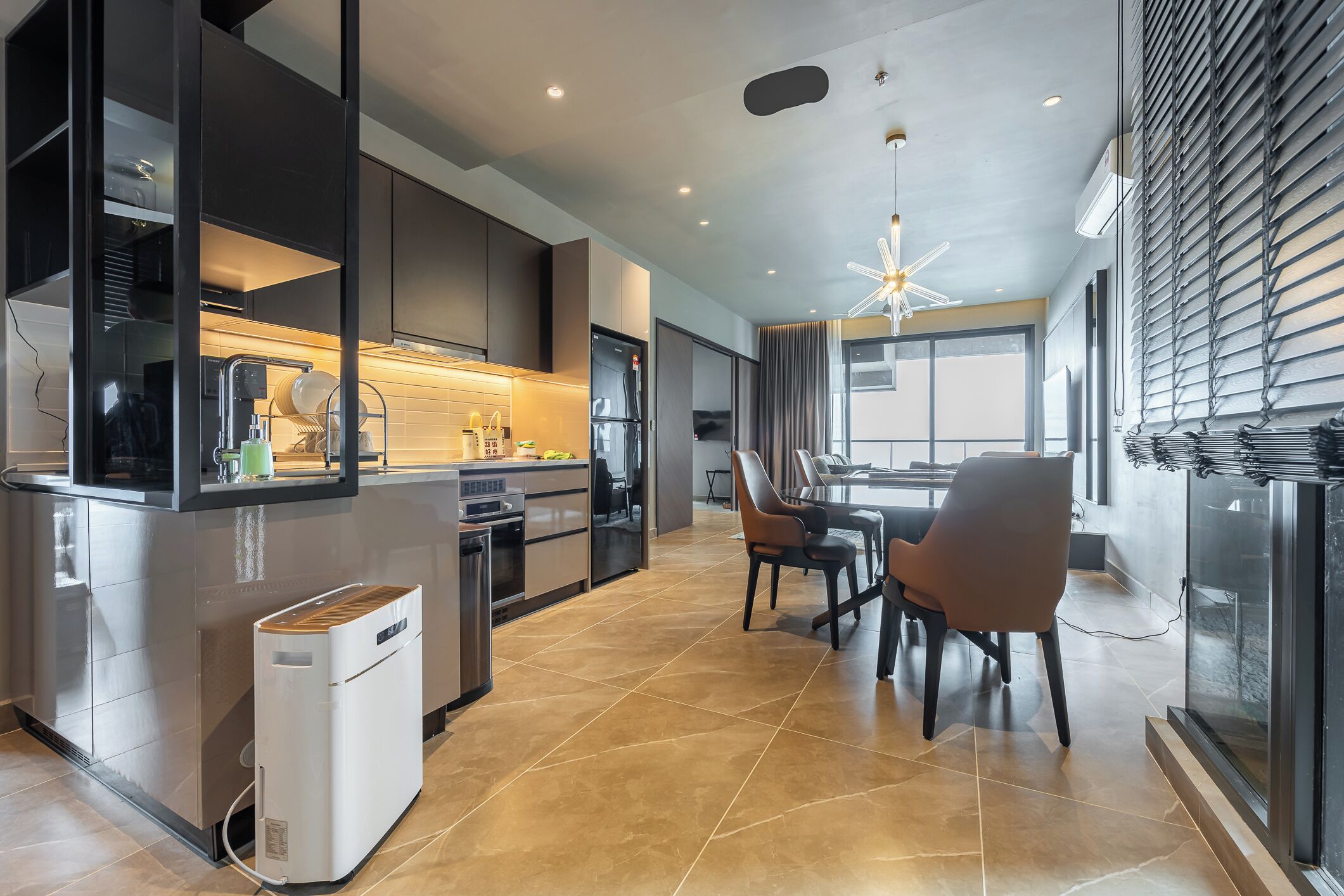 A modern kitchen with a built-in oven, a dining area with a table and chairs, and a large window with blinds.