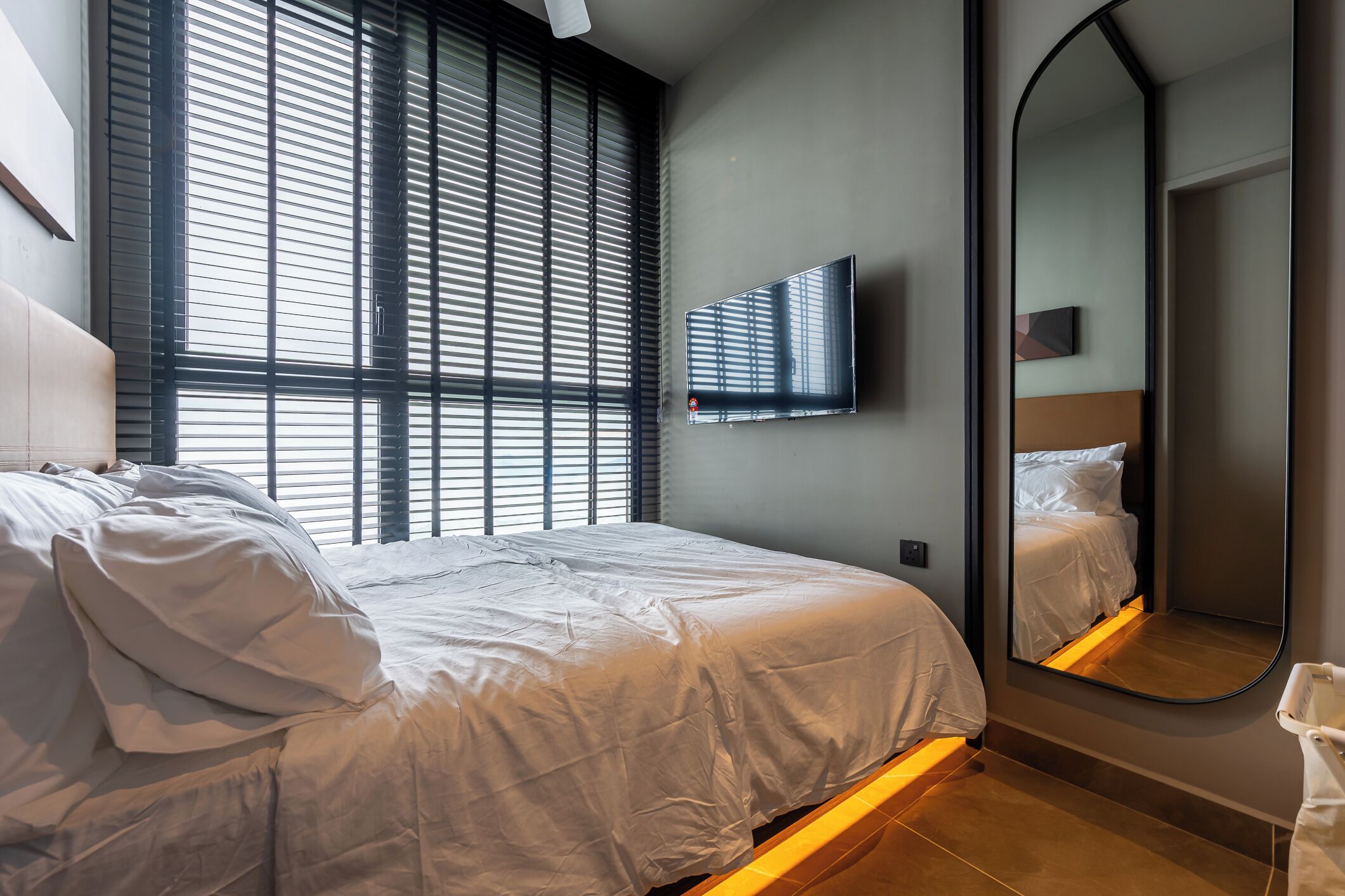 A modern bedroom with a large bed, a flat-screen TV mounted on the wall, and a large mirror.