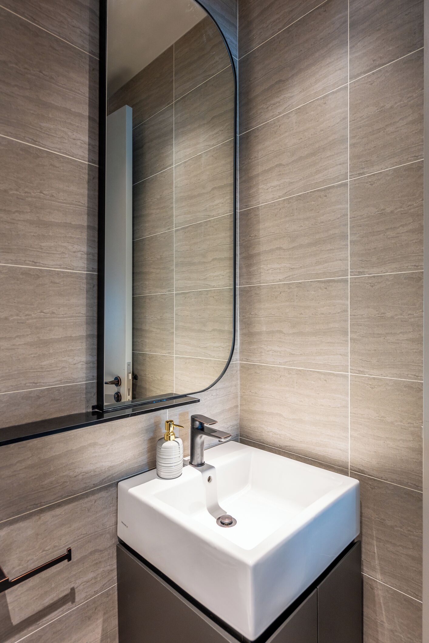 A modern bathroom with a large mirror, a white sink, and a towel dispenser.