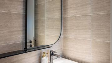 A modern bathroom with a large mirror, a white sink, and a towel dispenser.