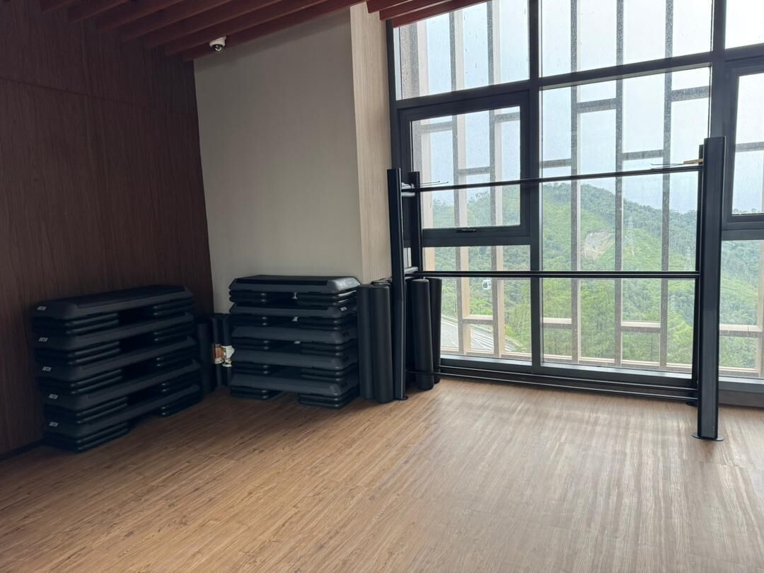 A room with a large window, wooden flooring, and stacks of black mats.