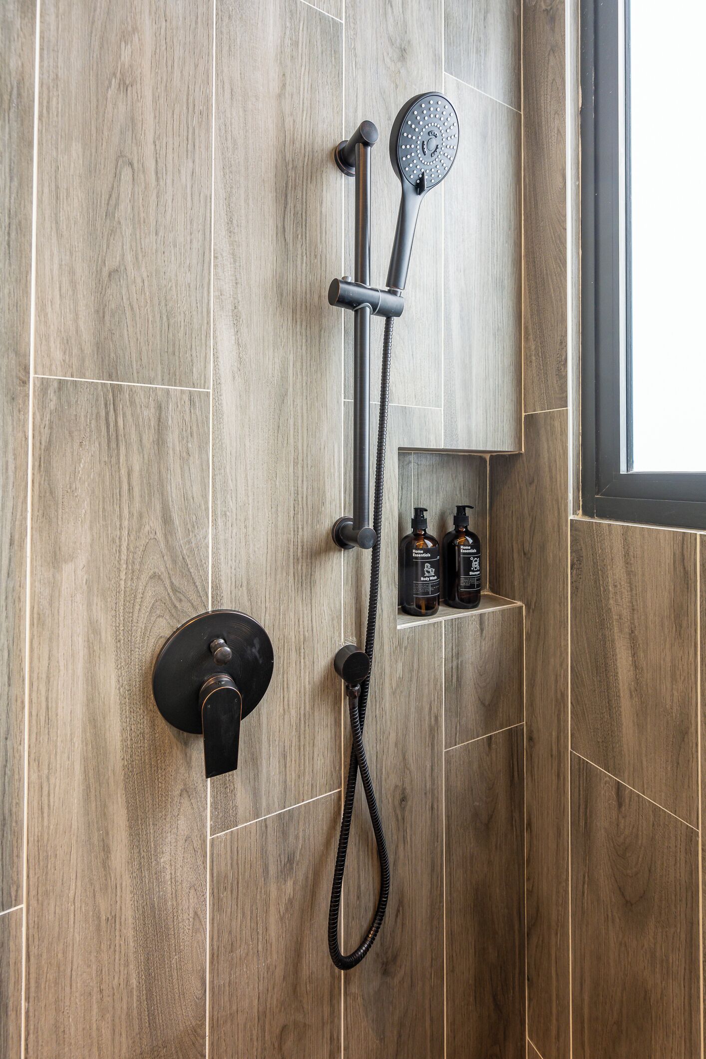 A shower with a handheld showerhead and a wall-mounted control. There are two bottles of shampoo and conditioner on a shelf below the shower.